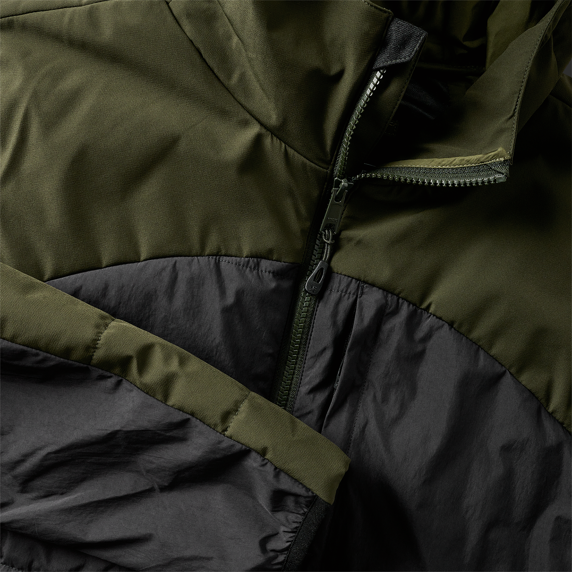 Close-up of the zippered front on a green and black hooded puffer jacket, showcasing high-quality construction.