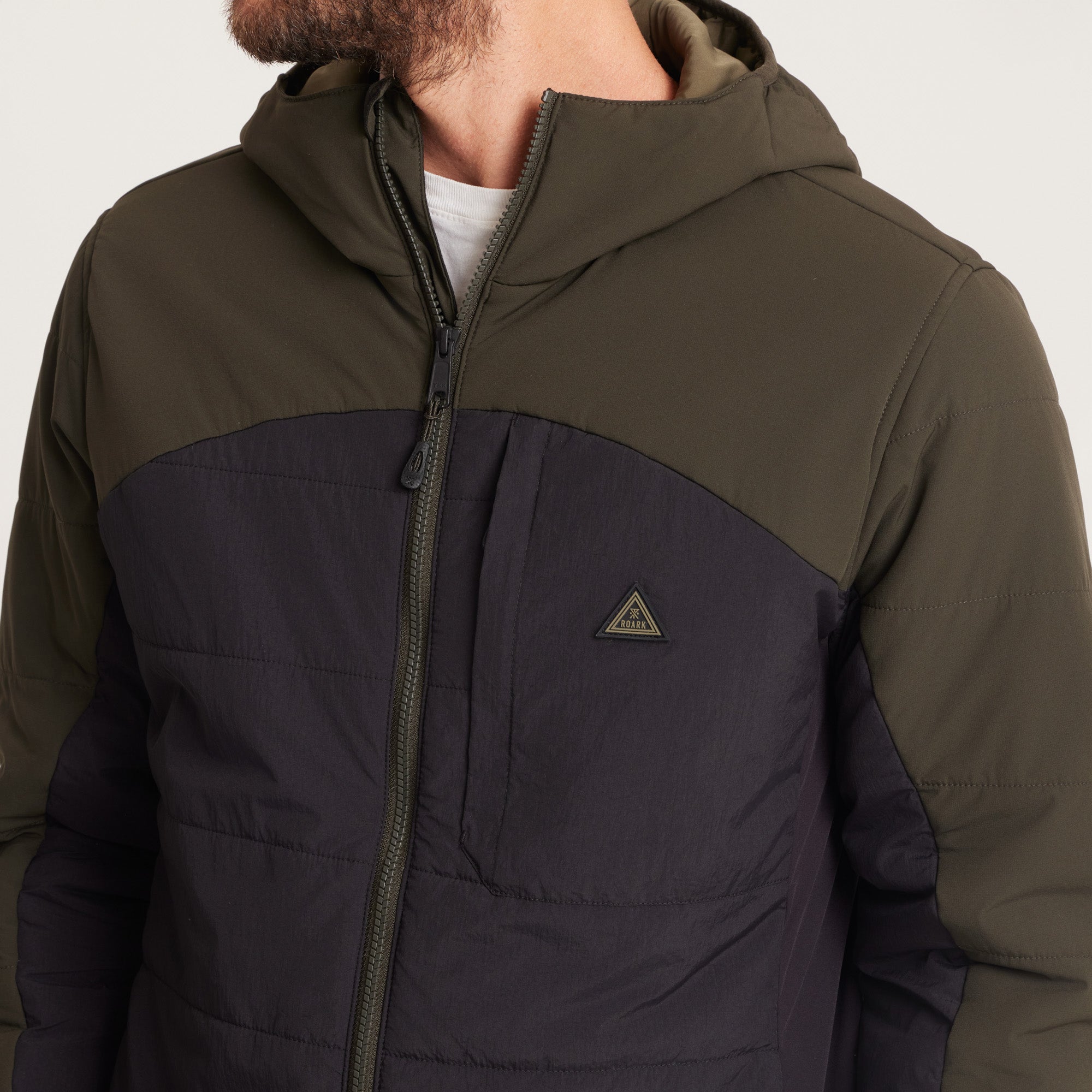 Close-up of a man wearing a green and black hooded jacket with a logo detail on the chest.