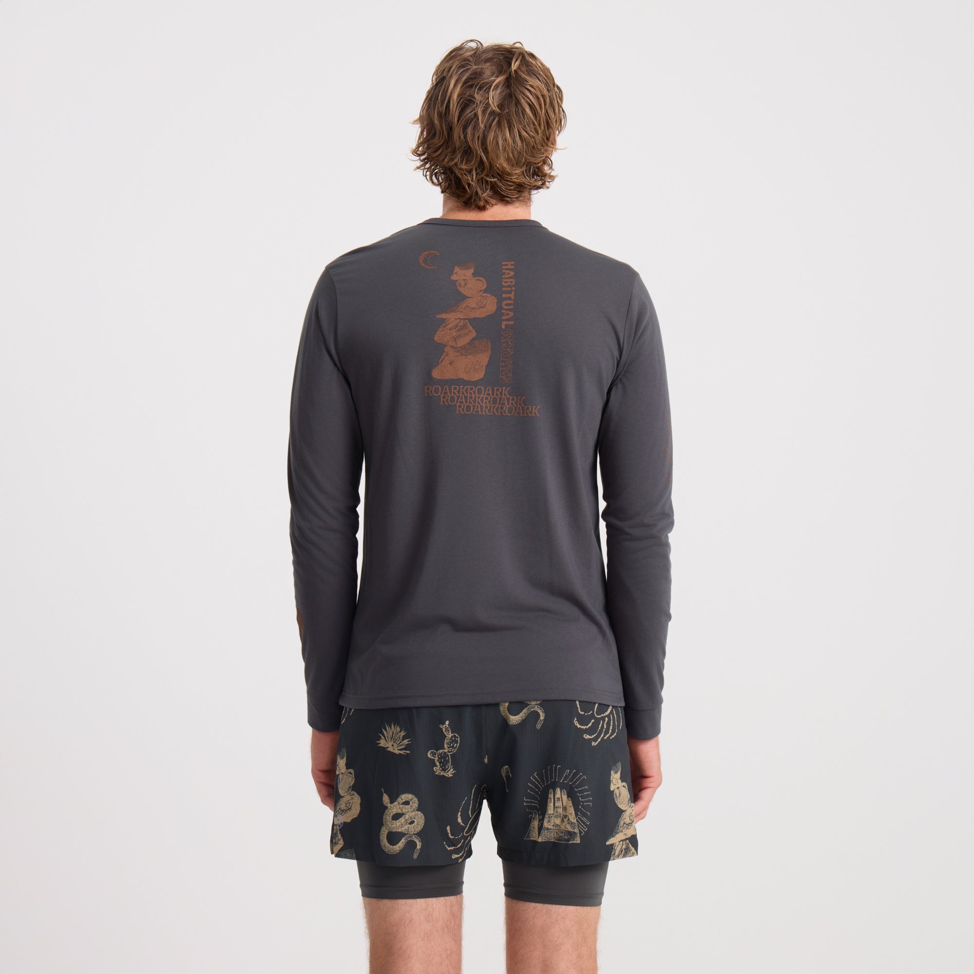Adventurous man wearing a long-sleeved active shirt and boardshorts by Roark, ideal for outdoor activities and travel.