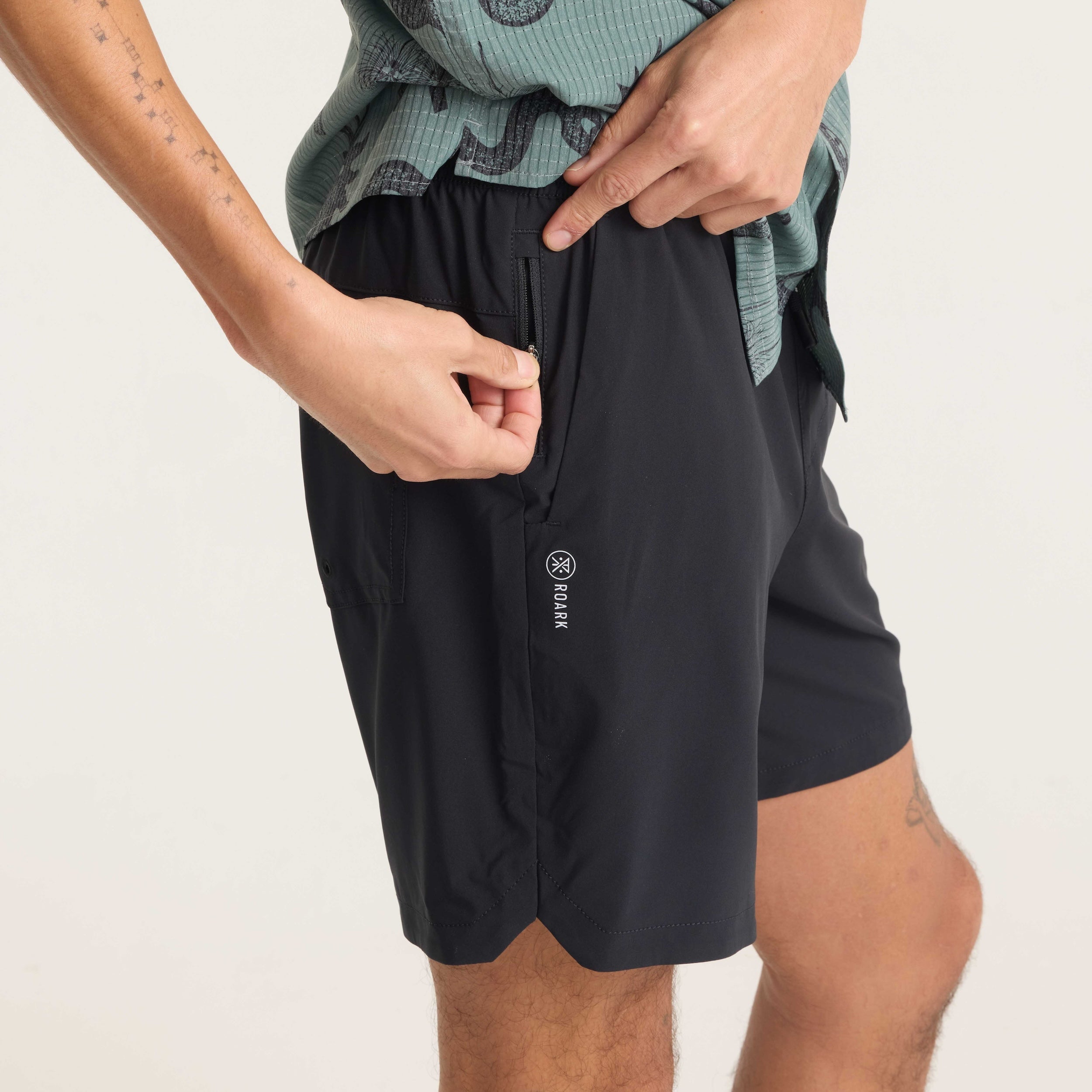 Model demonstrating the use of the side zip pocket on black Serrano shorts, highlighting secure storage and practical design.