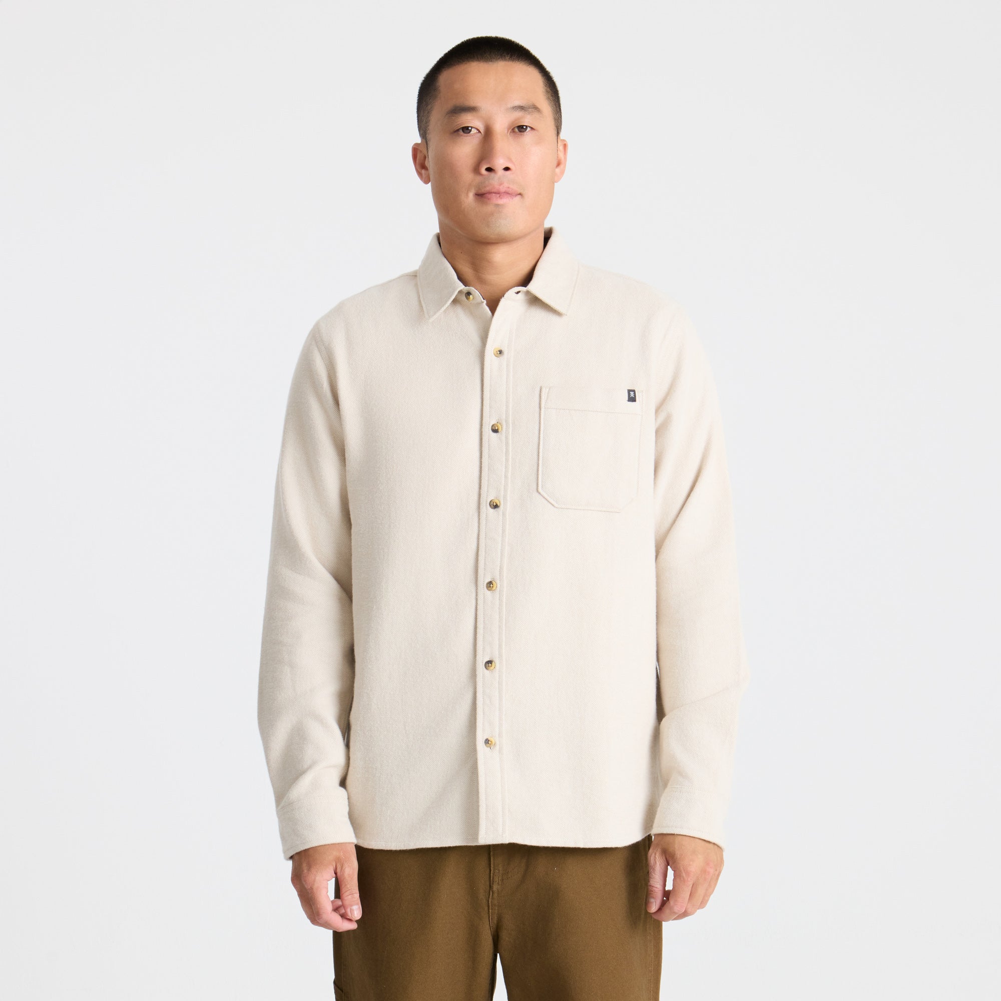 Man in Roark RW665 adventure gear standing on a forested summit overlooking a valley at sunset, embodying the spirit of exploration and travel.