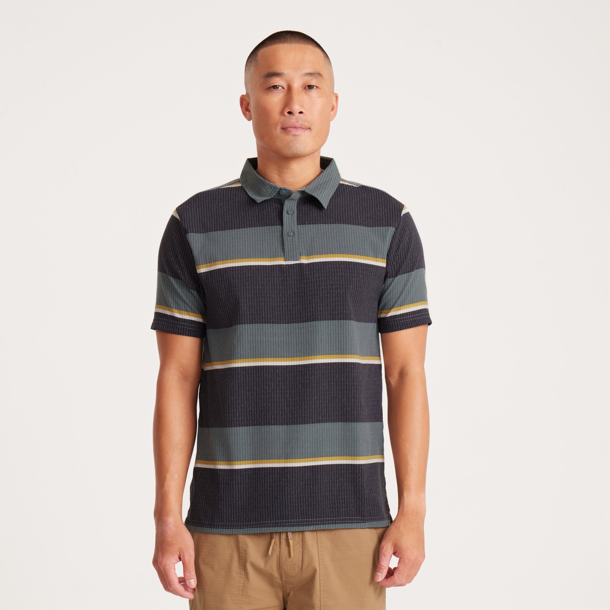 Model wearing a striped performance polo shirt in black and green tones, designed for comfort and style, perfect for everyday wear.