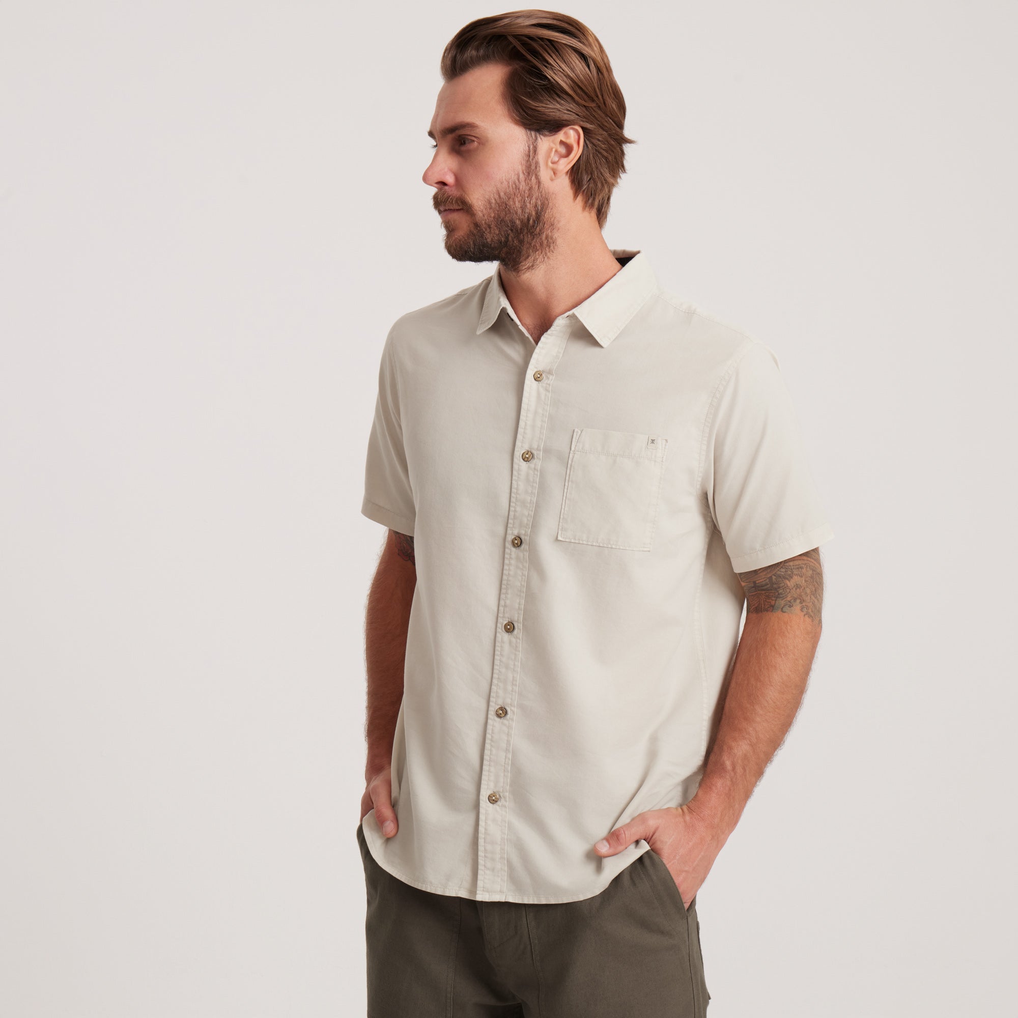 Side profile of a man wearing an off-white short-sleeve button-down shirt, showcasing a comfortable fit and modern styling.