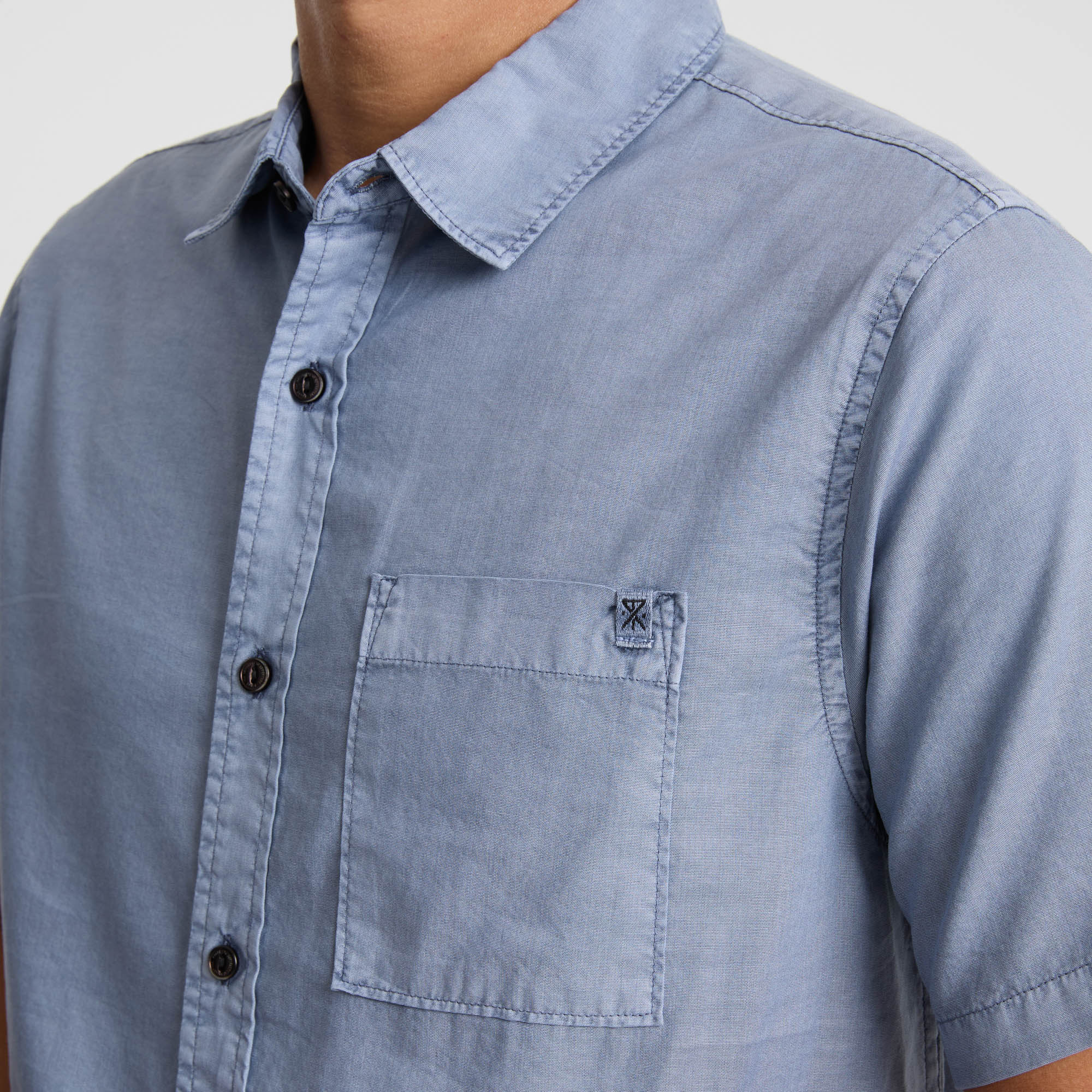 Detail of a linen Roark shirt featuring a collar, button, and pocket, ideal for outdoor and travel adventures.