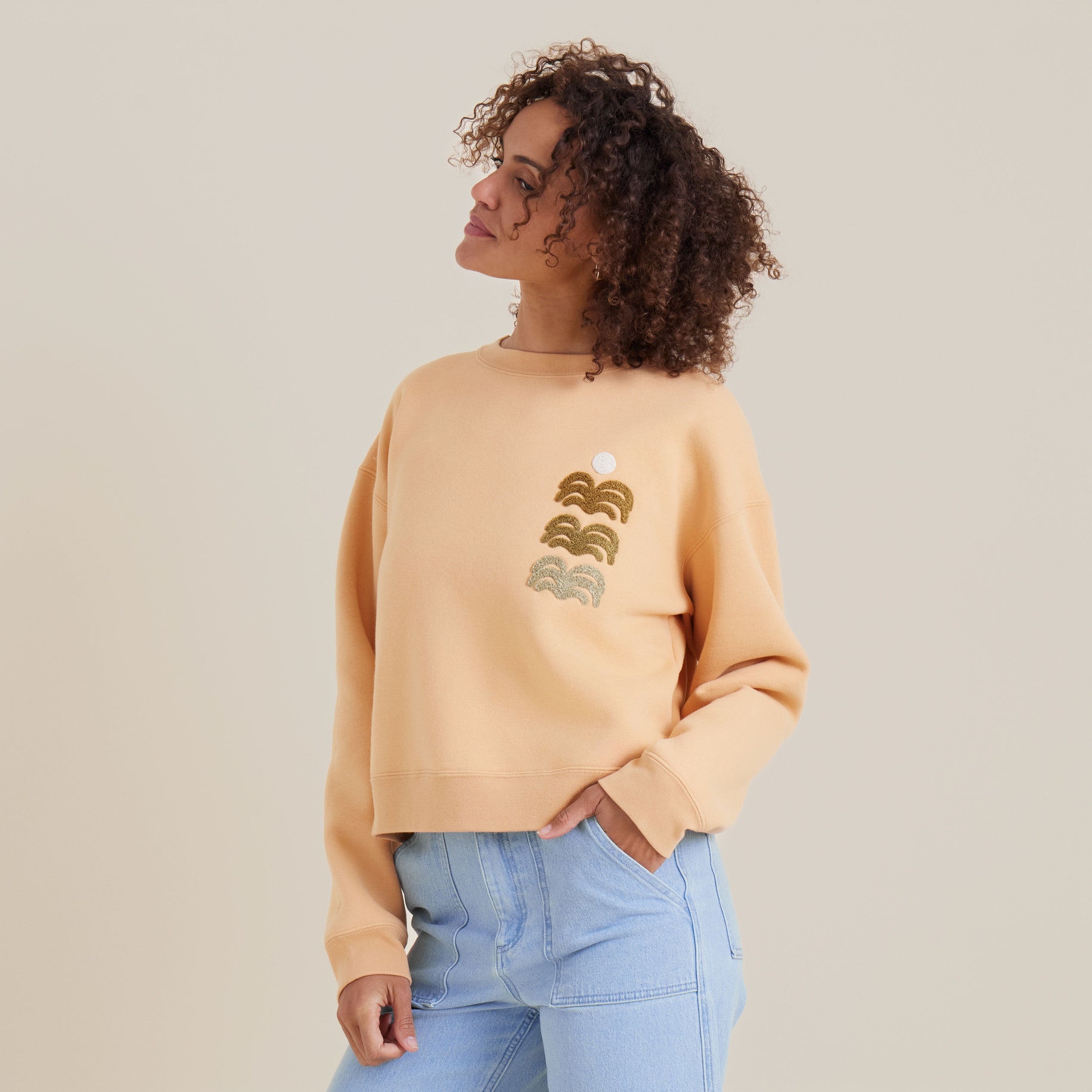 Side view of a woman in a peach crewneck sweatshirt and light blue jeans, highlighting a comfortable and trendy casual look.