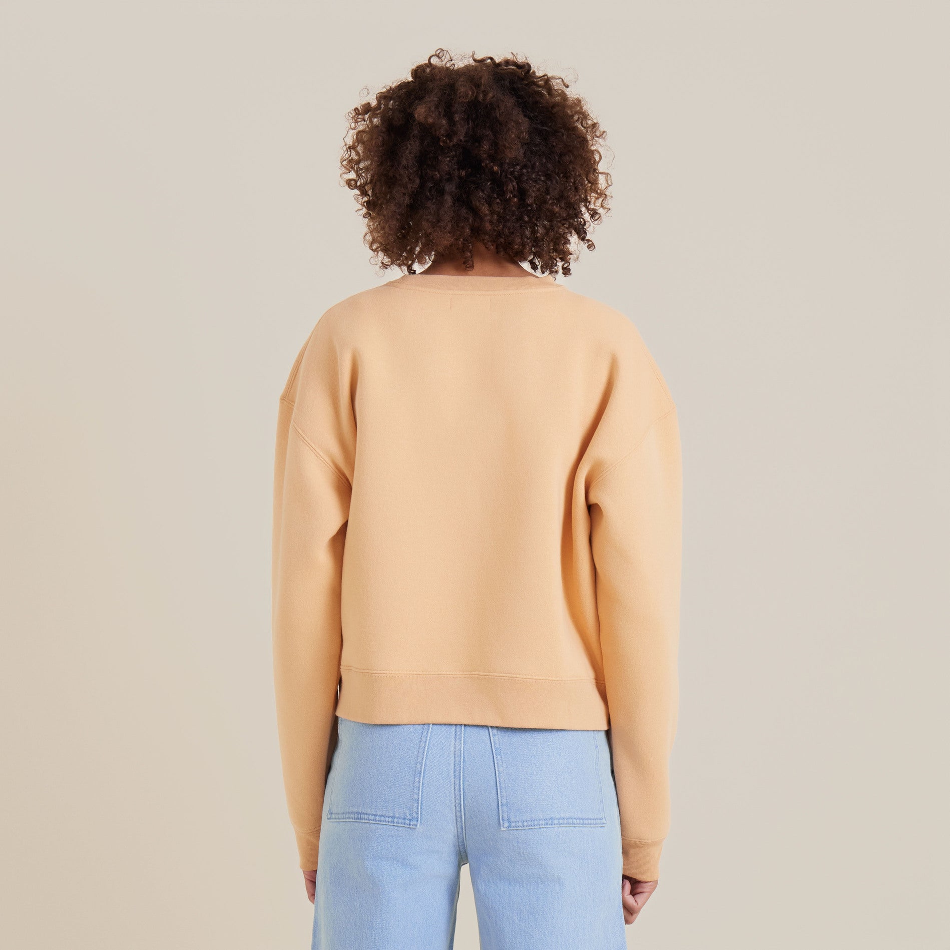 Back view of a peach crewneck sweater paired with wide-leg denim, showcasing the garment's simplicity and relaxed fit.
