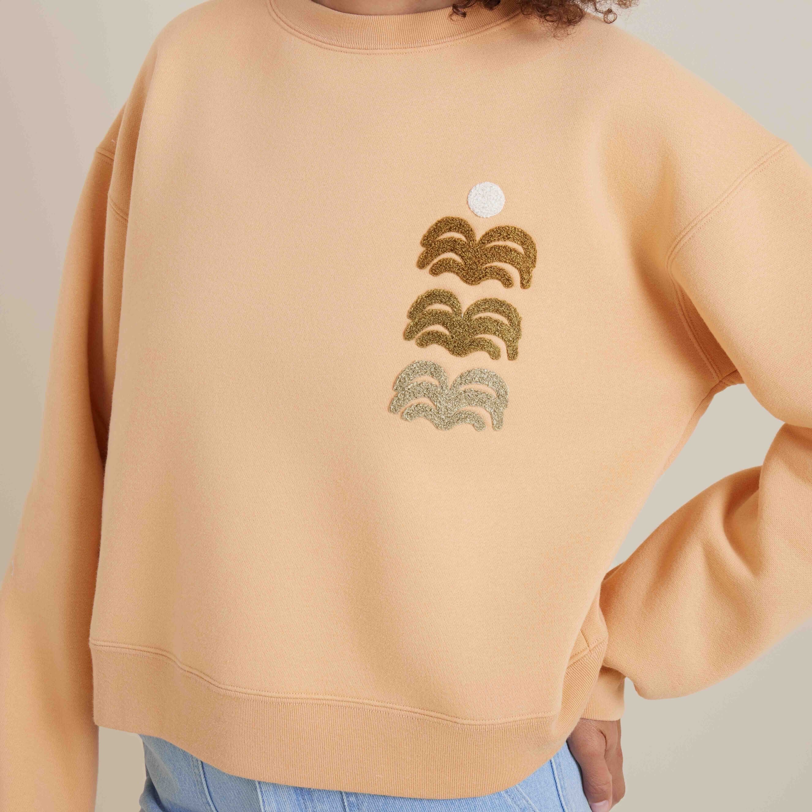 Close-up of embroidered waves on a light orange sweatshirt, adding a unique and stylish detail to the cozy casual wear.