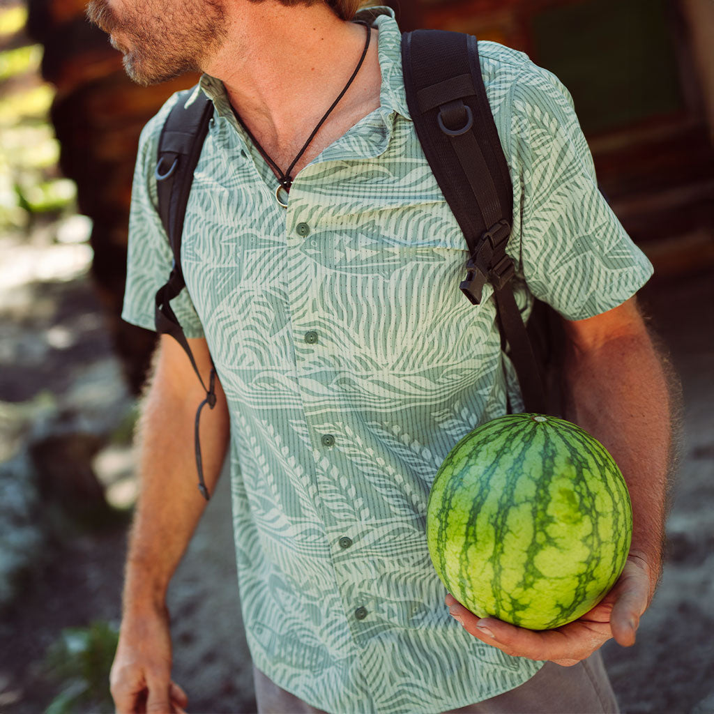 Man in a lightweight, fish pattern shirt, holding a watermelon outdoors with a blurred background