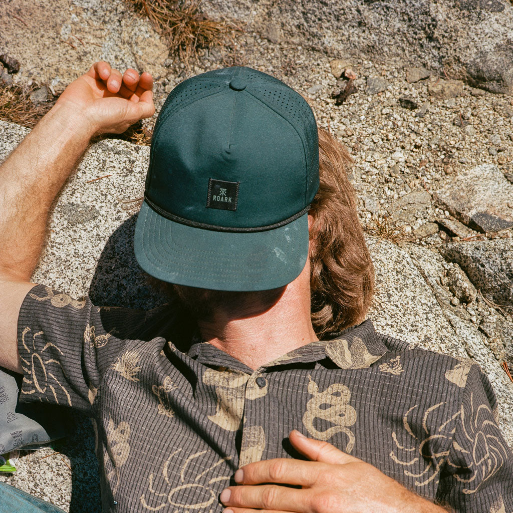 Person wearing a green cap and patterned shirt sitting on rocks