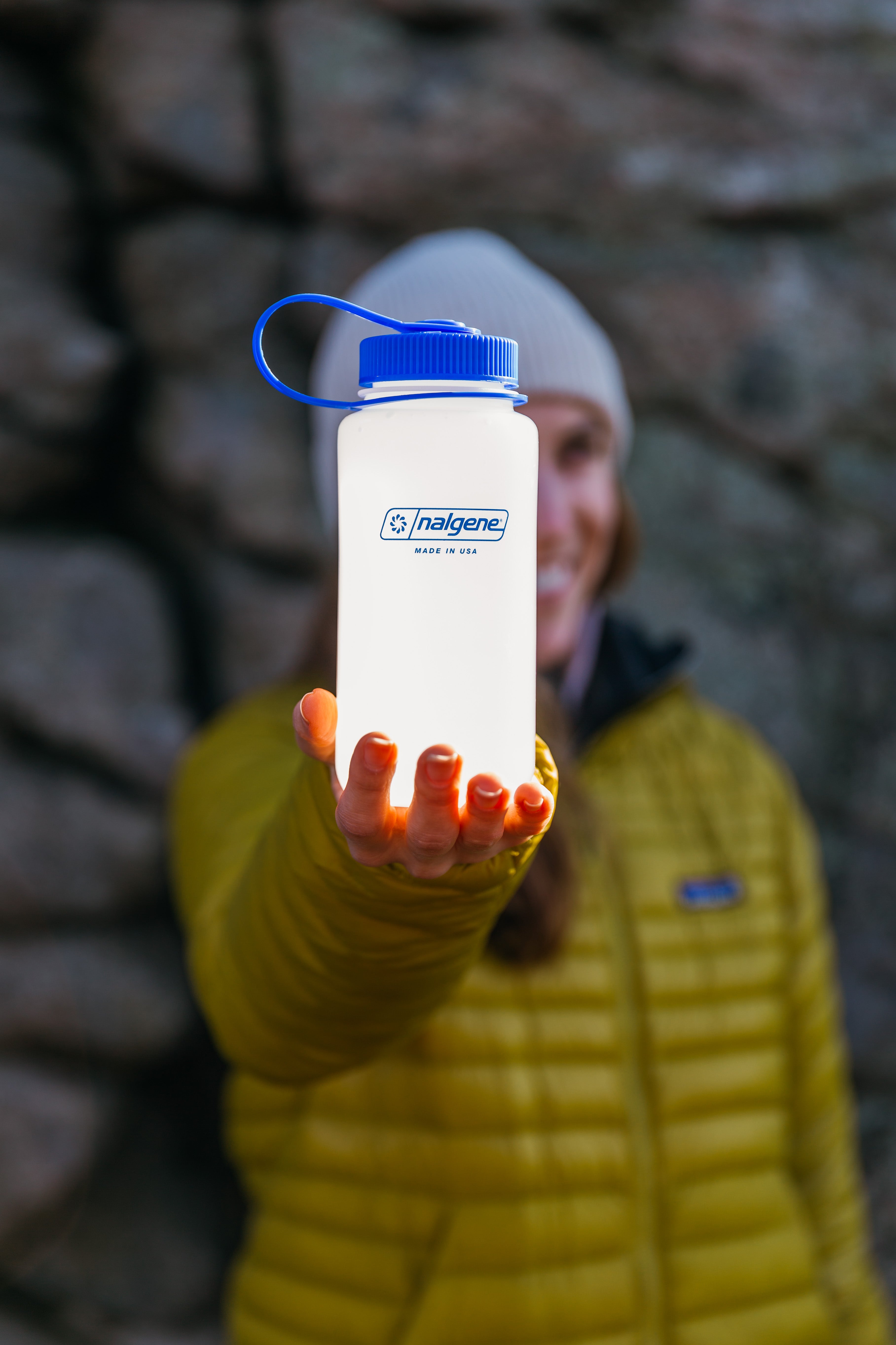 Person holding a Nalgene water bottle with a blue cap in front of a stone wall.