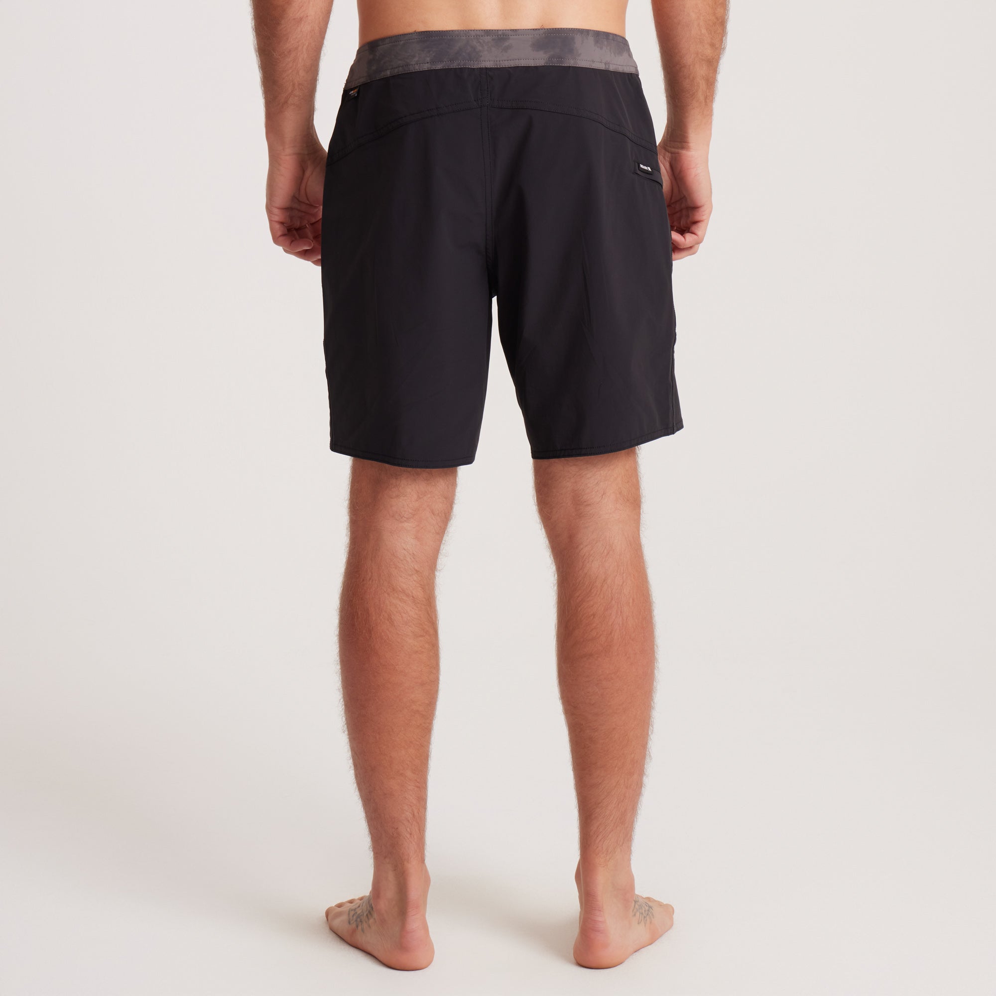 Back view of Roark black boardshorts showcasing a grey waistband and zippered pocket for utility and style.