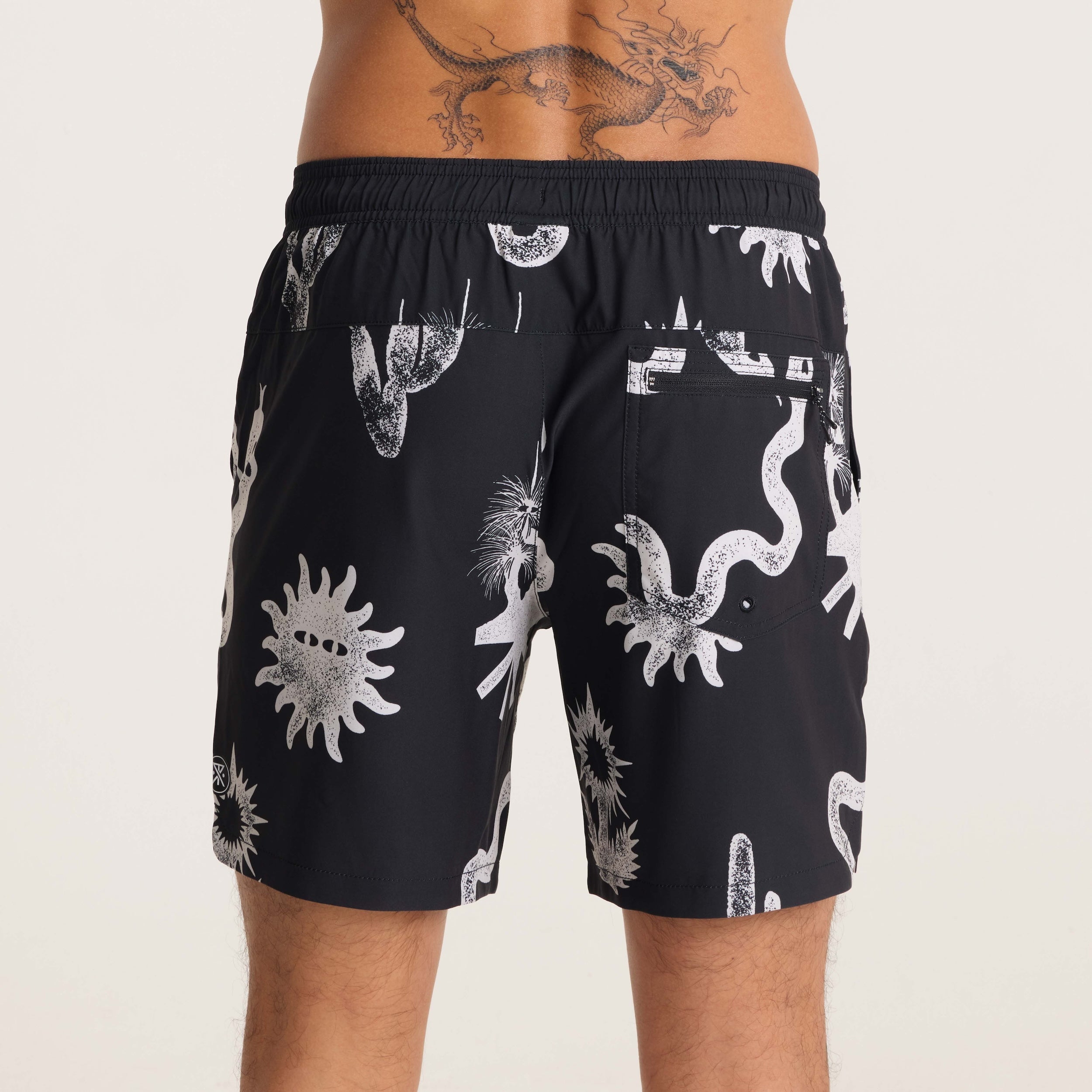 Model displaying the back of black swim shorts with intricate white desert-themed prints, styled for a casual and adventurous summer look.