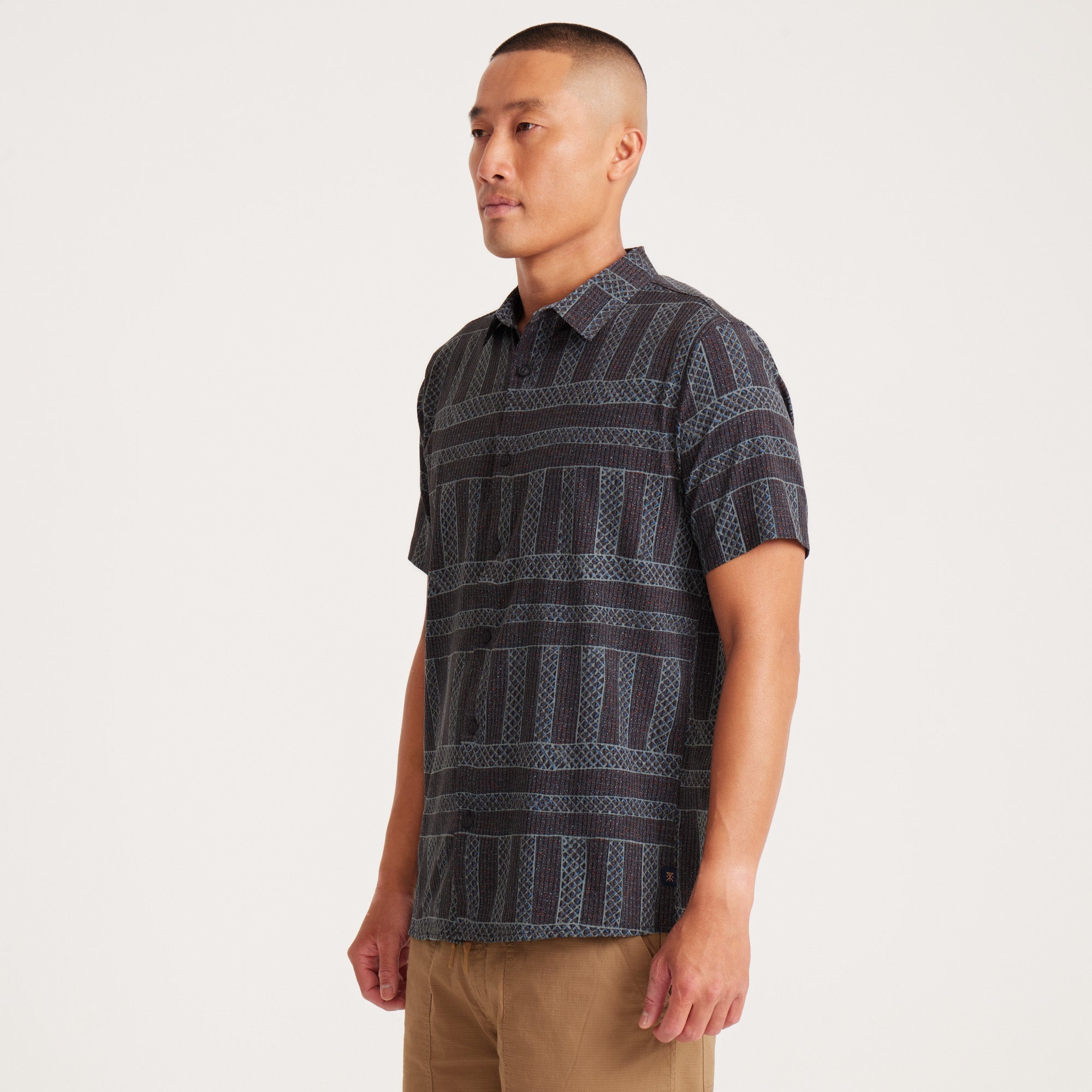 Side view of a model in a geometric-patterned shirt, showcasing sleeve and hemline details.
