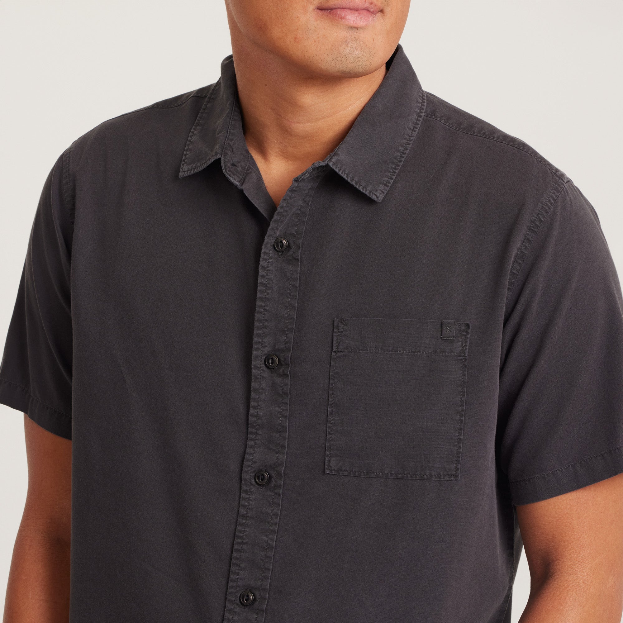 Close-up of the chest pocket and buttons on a black short-sleeve button-up shirt, highlighting the quality and detailing.