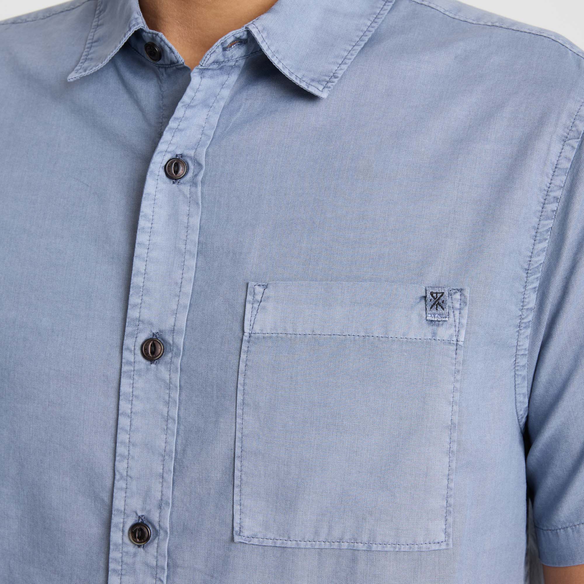 Close-up of a denim dress shirt featuring a pointed collar, button details, and chest pocket, embodying Roark's rugged adventure-ready style.