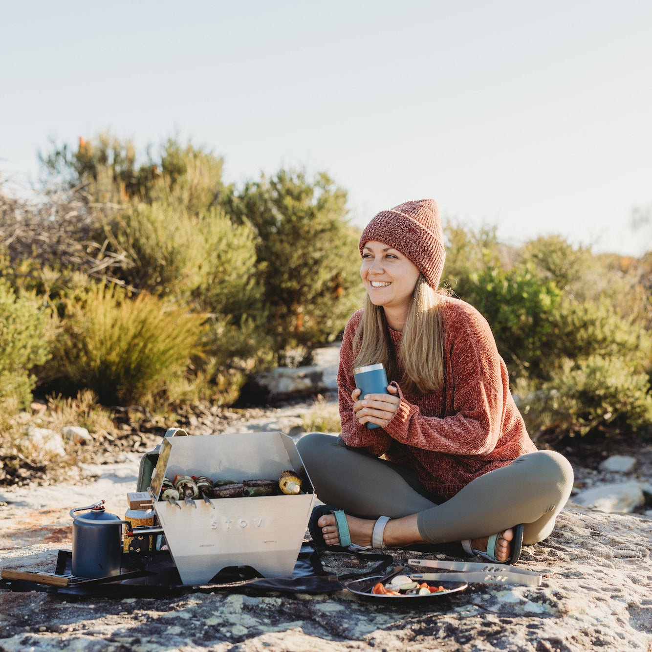 Woman bbqing on the compact STOV BBQ while holding a yeti cup