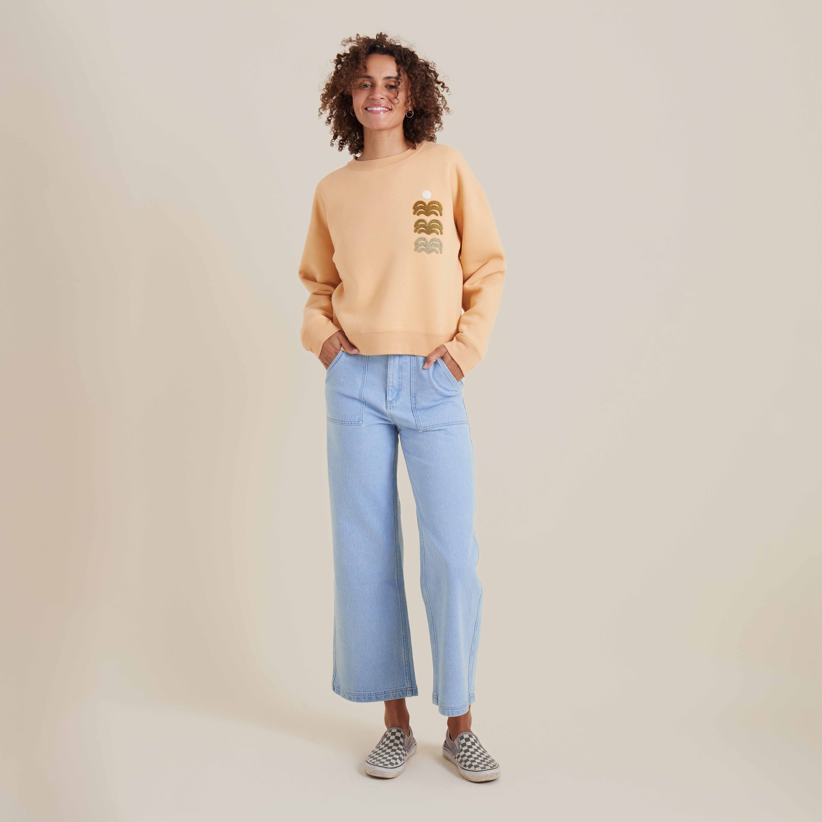 Woman in light orange crewneck sweater paired with wide-leg light blue jeans, showcasing a relaxed and casual outfit style.