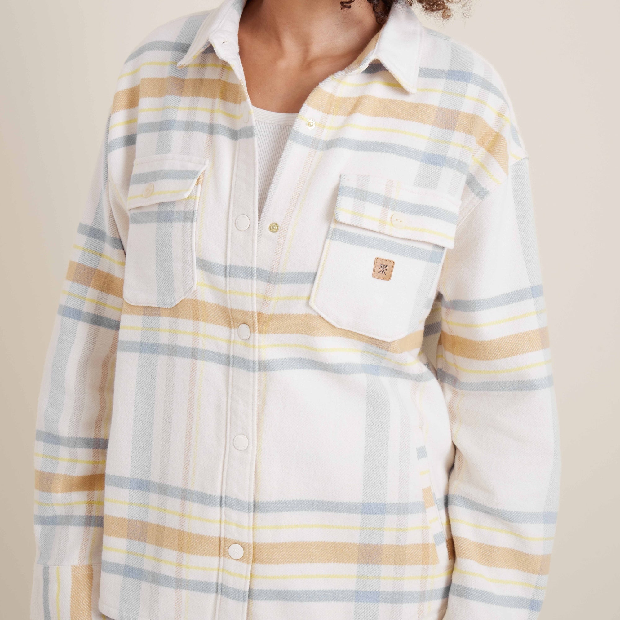 Close-up of the Amberley Dusk plaid shirt by Roark, featuring detailed chest pockets with a subtle logo patch and pastel plaid design.