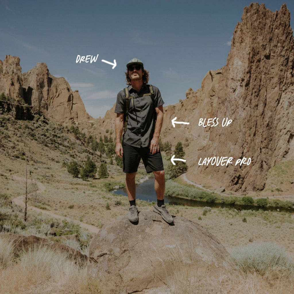 Man standing on a rock with mountainous landscape in the background, wearing outdoor gear.