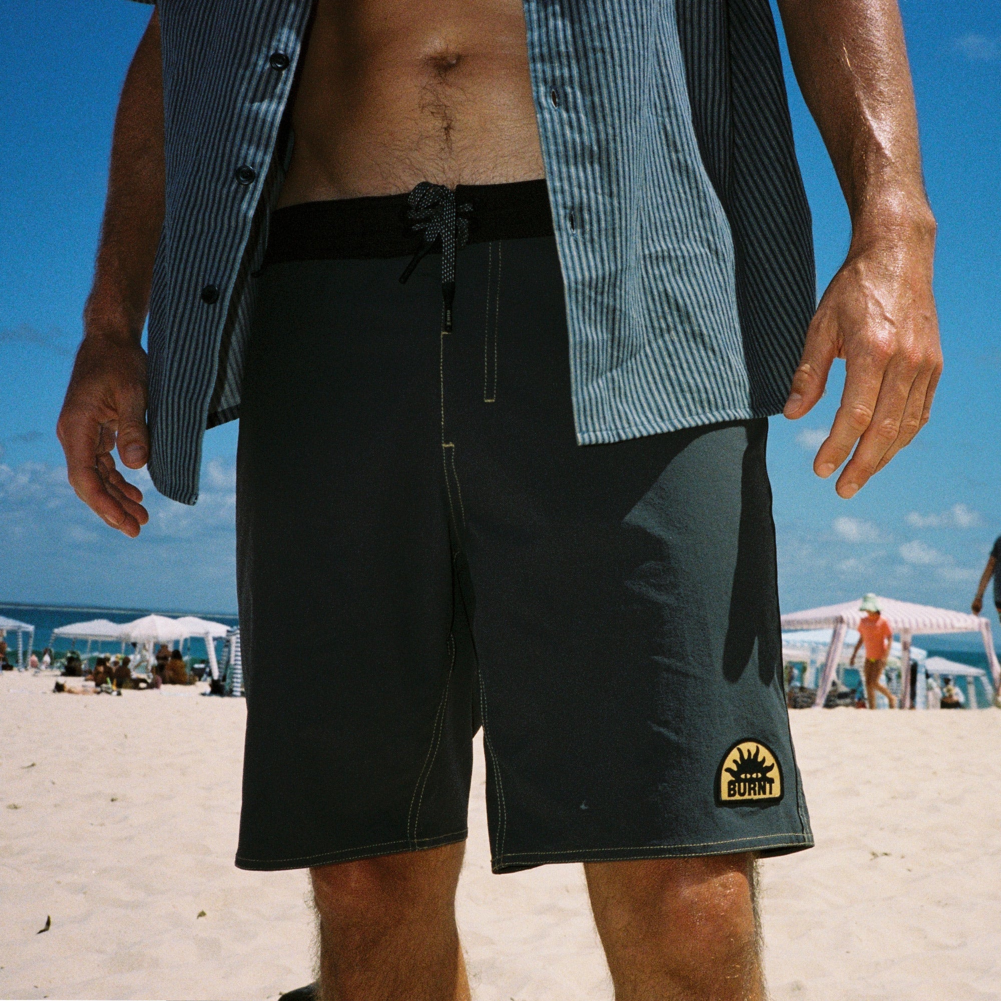 Person wearing grey board shorts with a burnt logo on a beach