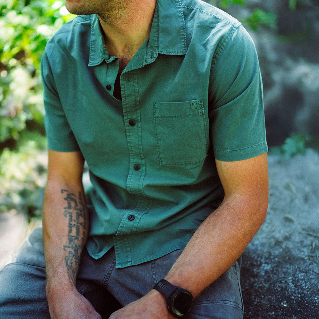 Person wearing a green shirt sitting outdoors with a natural background