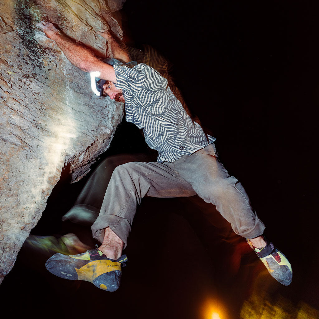 Person rock climbing in a dark cave with artificial lighting.